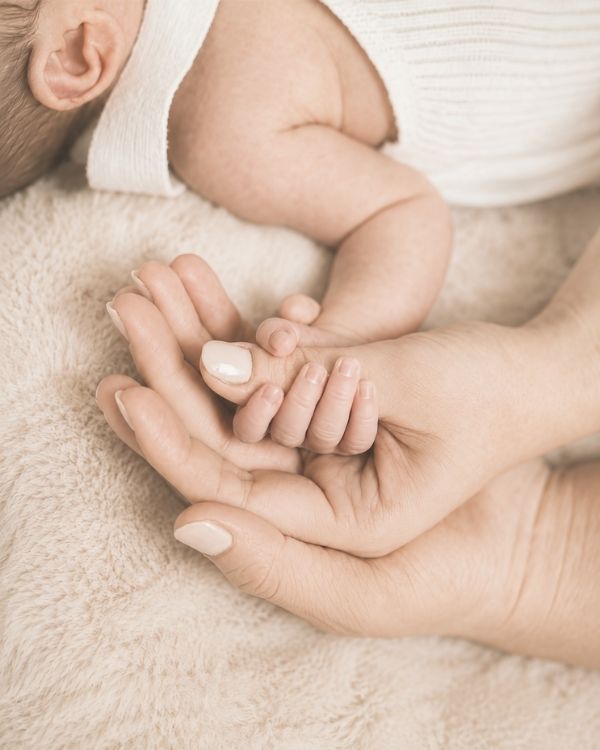 Parent holding newborn baby's hand in a soft, neutral setting